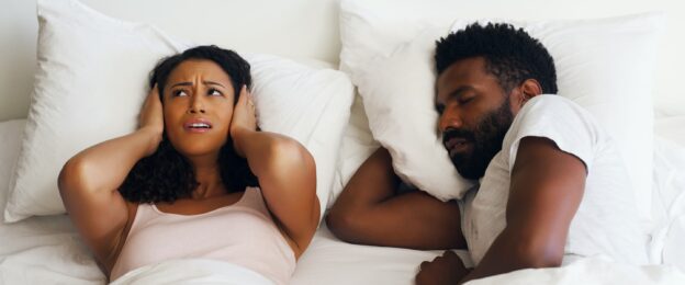 Couple in bed with one holding their hands over their ears
